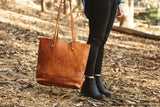 A woman holding a Tradevia Fore Street Tote Bag in the woods.