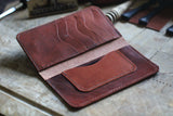 A WM Leatherwork Collection - Premium Leather Field Notes Wallet from Tradevia lies open on a wooden surface, showcasing several card slots and a pocket. Various leatherworking tools are scattered in the background.