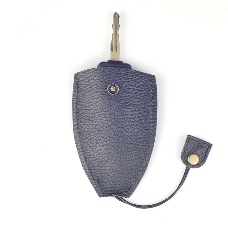 A key partially inserted in a Rogue Leather Key Protective Case by Tradevia, featuring a black textured durable cowhide with a snap button and dangling flap.