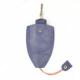 A car key with a black head is partially inserted into a Rogue Leather Key Protective Case by Tradevia, which has an orange string with a snap button closure.