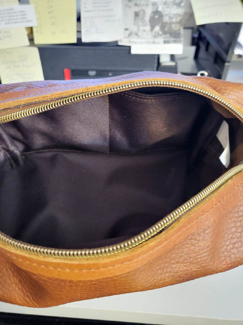 Unzip the Tradevia Leather Dopp Kit in brown to reveal its dark fabric-lined interior, highlighting an empty main compartment made from genuine leather.