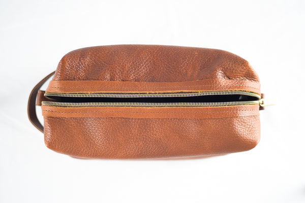 Top view of a Tradevia Leather Dopp Kit, crafted from genuine leather, featuring a visible zipper and handle, set against a white background.