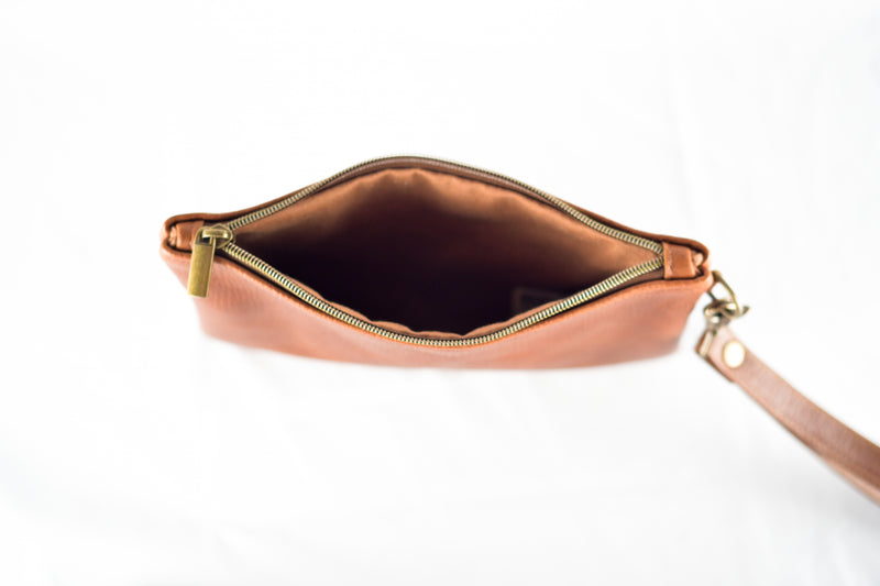 A top-down view of an open Tradevia Leather Clutch from the Fore Street Tote Bag and Clutch Bundle, crafted from full-grain leather with a zipper and wrist strap, set against a white background.