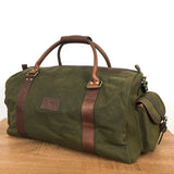 A White Cap Waxed Canvas Duffle from Tradevia, crafted from water-resistant waxed canvas and featuring brown full-grain leather straps, two handles, and a shoulder strap, placed on a wooden surface.