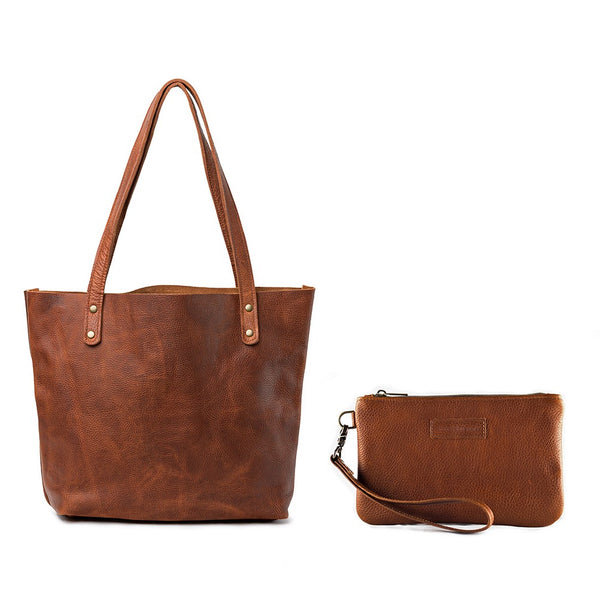 Fore Street Tote Bag by Tradevia, a brown leather tote bag with a matching wristlet pouch, crafted in Maine from luxurious full-grain leather and set against a white background.