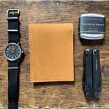 A Heritage Wallet in Baseball Glove Leather made by Tradevia, watch, and other items on a wooden table.