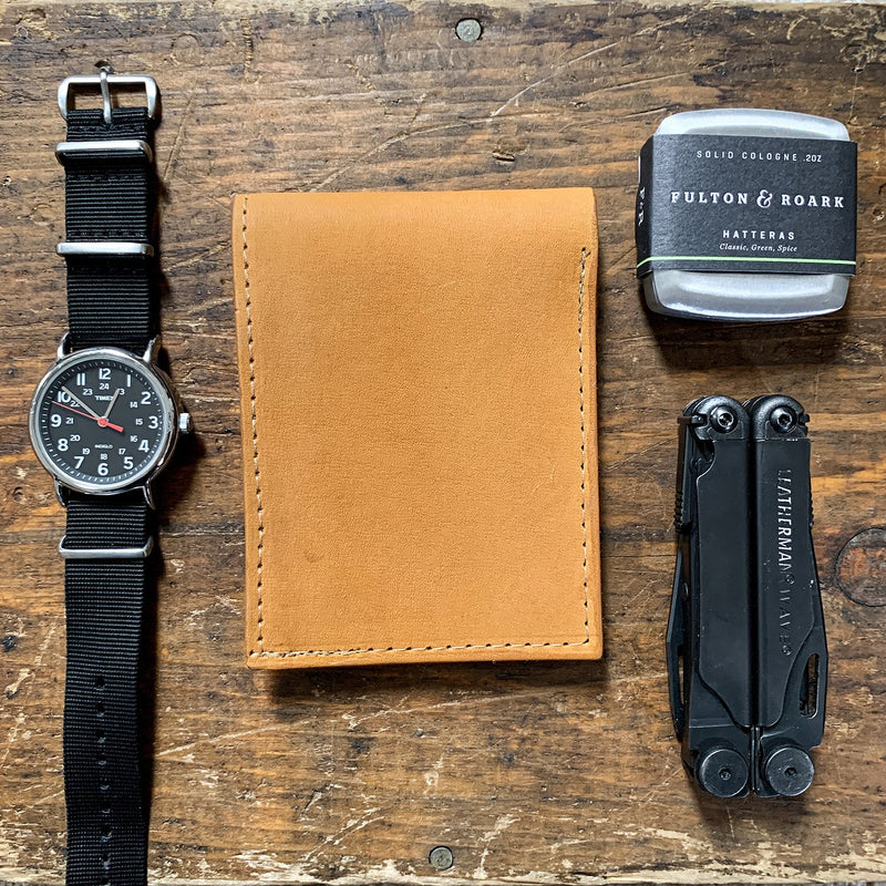 A Heritage Wallet in Baseball Glove Leather made by Tradevia, watch, and other items on a wooden table.