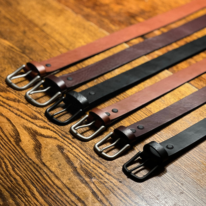 Five Tradevia Baxter Leather Belts - 1.5" Wide are lined up on a wooden table.