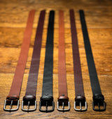 Five Chamberlain Leather Belts - 1.25" Wide by Tradevia are lined up on a wooden table.