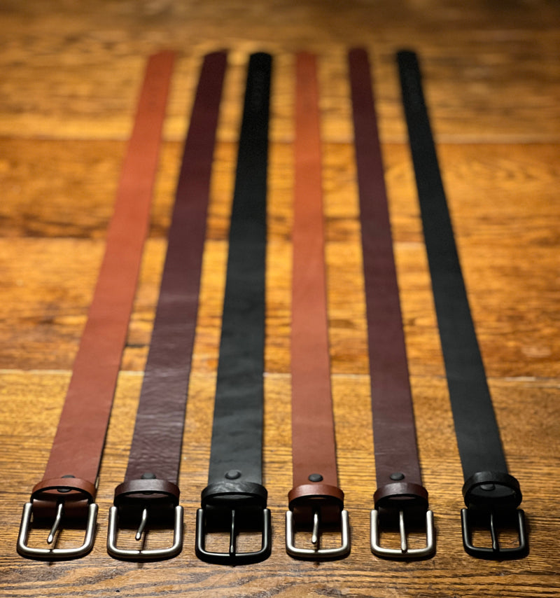 Five Chamberlain Leather Belts - 1.25" Wide by Tradevia are lined up on a wooden table.
