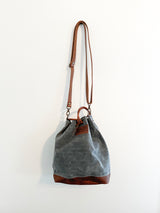 A small grey Tradevia Kennebunkport bucket bag hanging on a wall.