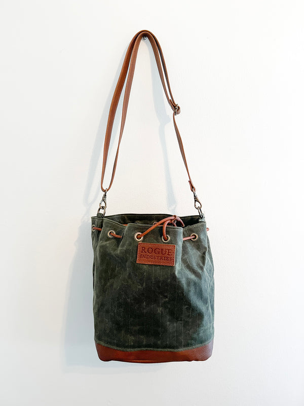 A green Tradevia Kennebunkport Bucket Bag hanging on a wall.