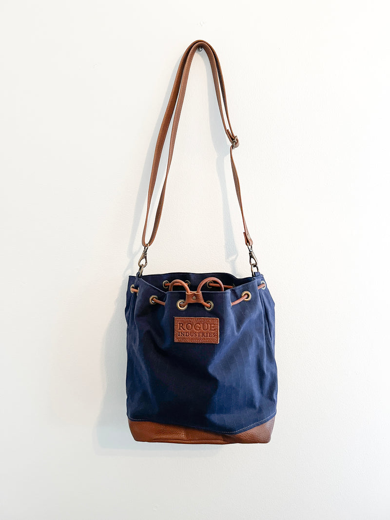 A blue Tradevia Kennebunkport Bucket Bag hanging on a wall.