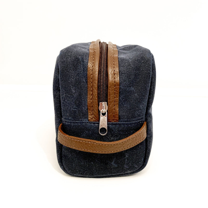 A durable, blue and tan Tradevia Waxed Canvas Dopp Kit on a white surface.