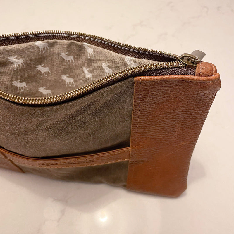 A brown and tan waxed canvas pouch with a deer on it, the Eastport Clutch by Tradevia.