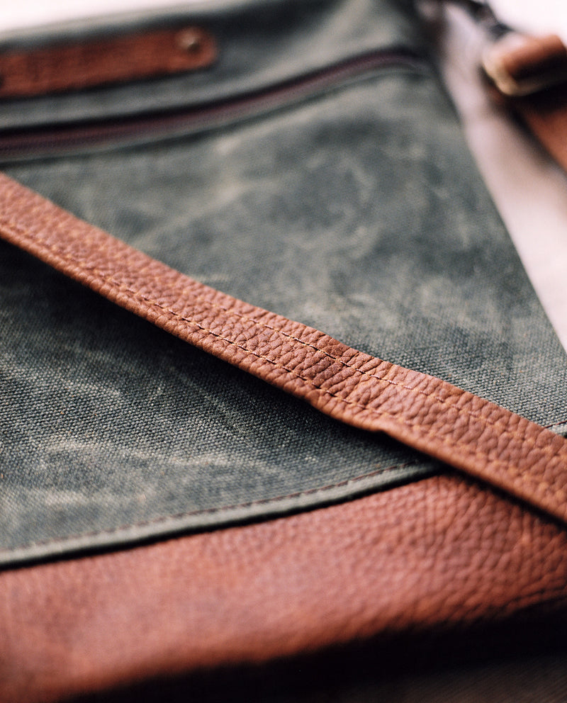 A green and brown waxed canvas and cowhide Tradevia Ellis River Crossbody Bag.