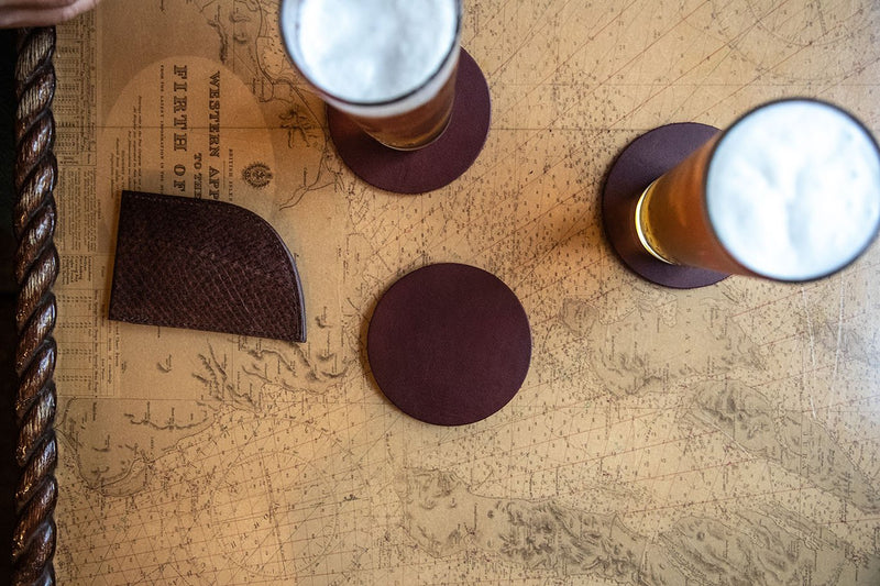 Two glasses of beer on Sebago Camp Coasters from Tradevia rest on a table next to a map.