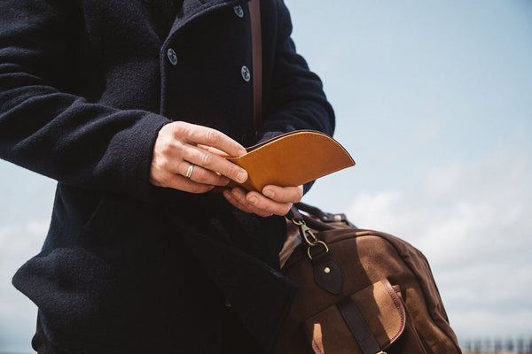 A man is holding a brown leather RFID-blocking Rogue Front Pocket Wallet in Ballglove from Tradevia.