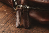 A brown Tradevia Katahdin Leather Briefcase with a removable strap on a wooden table.