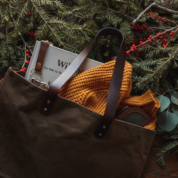 A durable, brown Tradevia waxed canvas tote bag with top-grain leather straps.