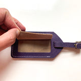 A person is holding a purple Tradevia cowhide leather luggage tag.