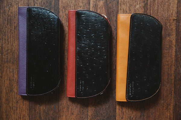 A group of Tradevia RFID Blocking Clutch - Ostrich Print cases on a wood surface.