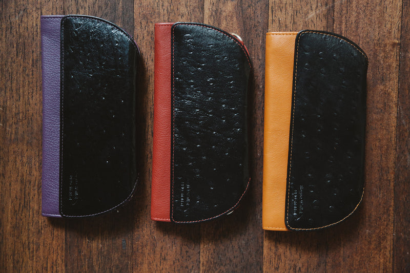 A group of Tradevia RFID Blocking Clutch - Ostrich Print cases on a wood surface.