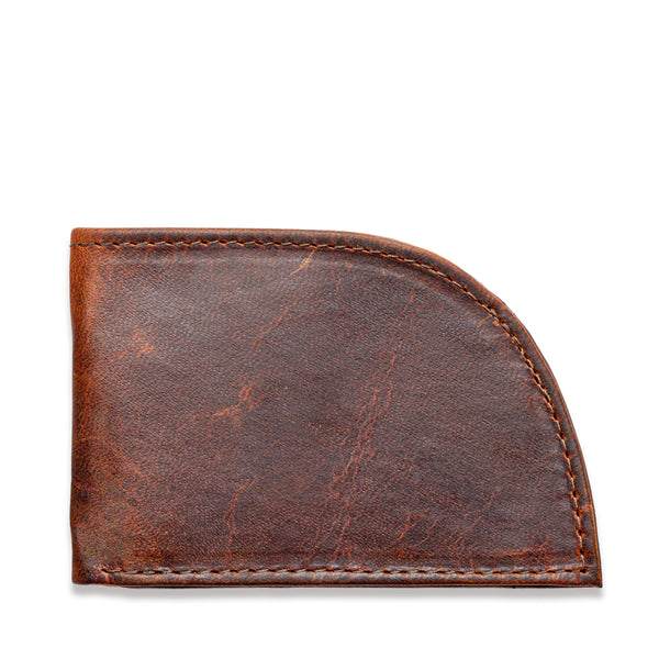 A weathered brown leather slim wallet, the Factory Second PREVIOUSLY EMBOSSED Made in Maine Front Pocket Wallet by Tradevia, features a curved bottom right corner and shows signs of wear and aging. The visible stitching around the edges adds to its rustic charm. This RFID-blocking wallet, crafted in Maine, is closed and appears empty.