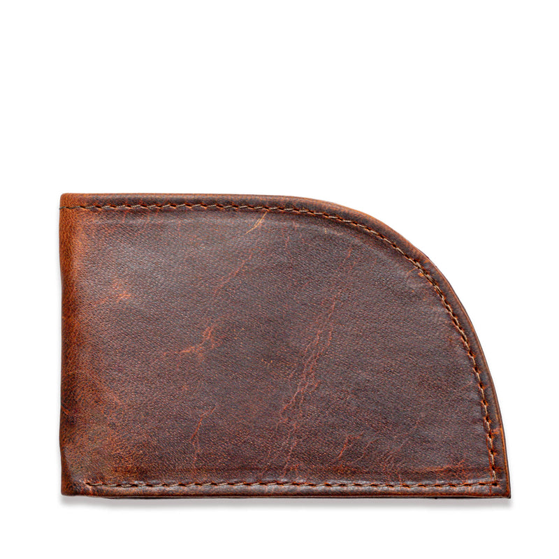 A weathered brown leather slim wallet, the Factory Second PREVIOUSLY EMBOSSED Made in Maine Front Pocket Wallet by Tradevia, features a curved bottom right corner and shows signs of wear and aging. The visible stitching around the edges adds to its rustic charm. This RFID-blocking wallet, crafted in Maine, is closed and appears empty.