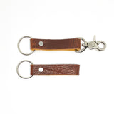 A pair of Tradevia brown leather keychains with nickel rivet on a white background.