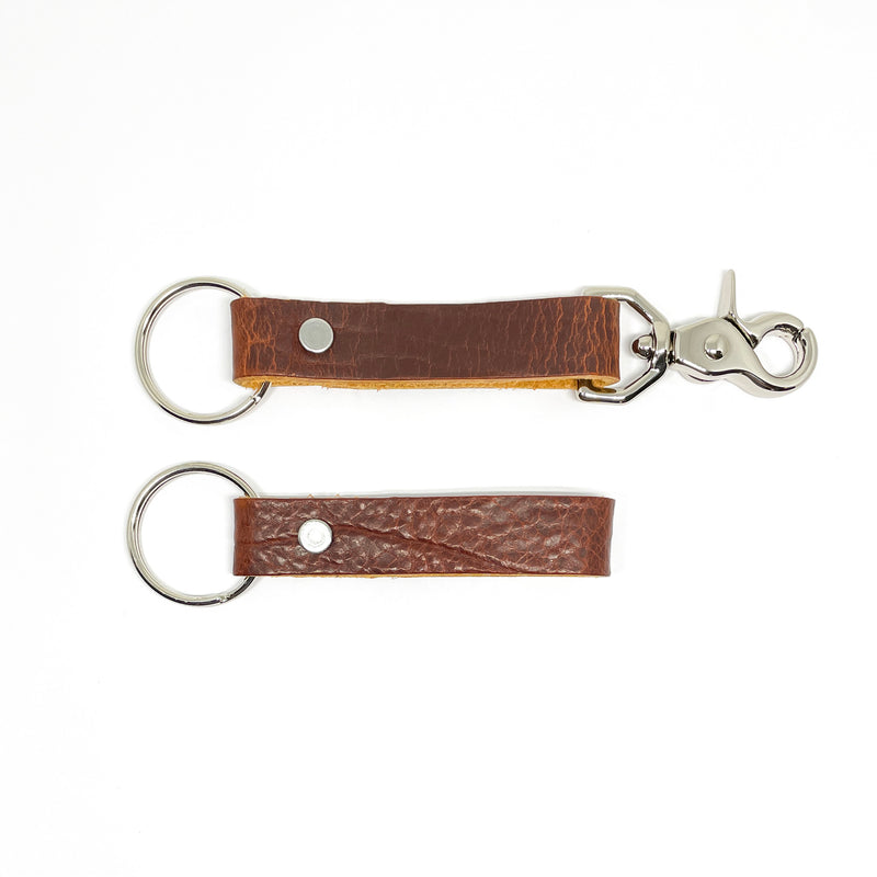A pair of Tradevia brown leather keychains with nickel rivet on a white background.