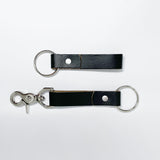 Two durable Tradevia black leather keychains on a white surface.