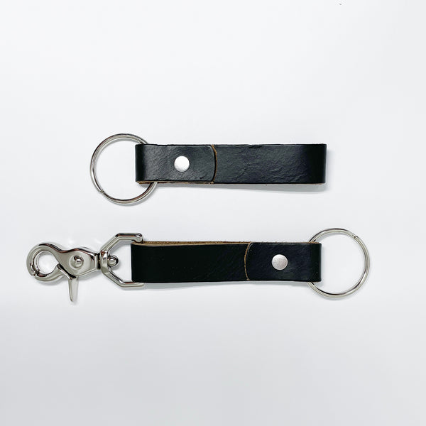 Two durable Tradevia black leather keychains on a white surface.