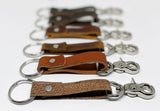 A row of different colored durable Tradevia leather keychains on a white surface.