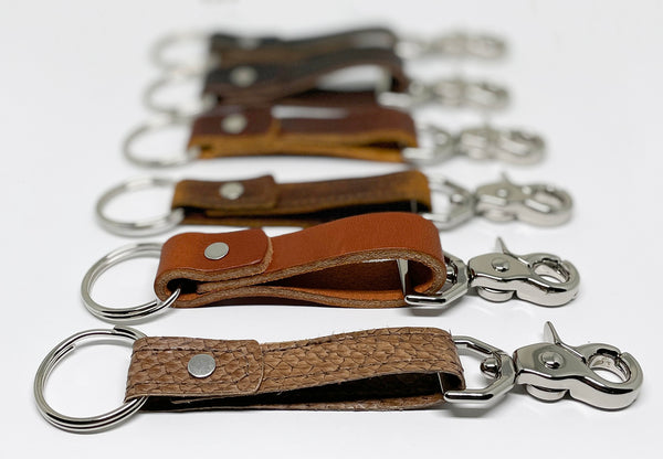 A row of different colored durable Tradevia leather keychains on a white surface.