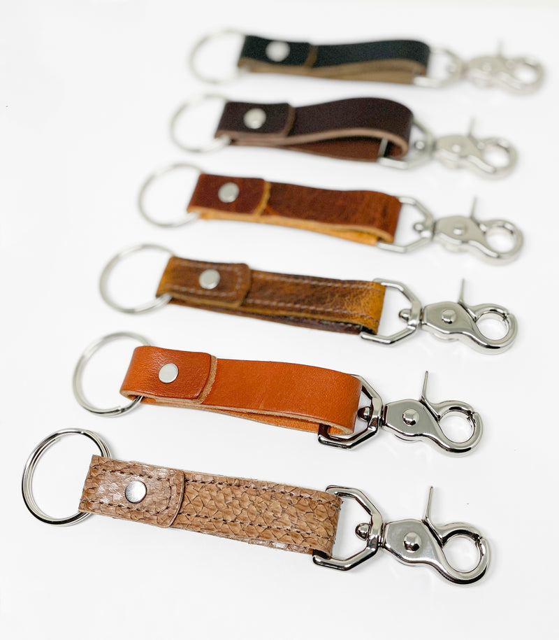 A row of different colored, Tradevia Leather Key Chains on a white surface.