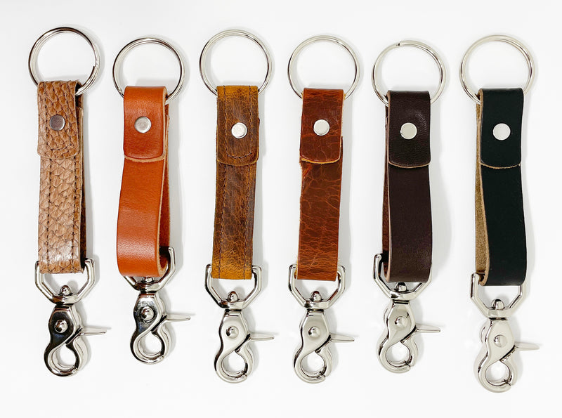 A row of different colored, durable Tradevia leather keychains on a white background.