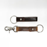 Two Tradevia brown leather keychains with a nickel rivet on a white background.
