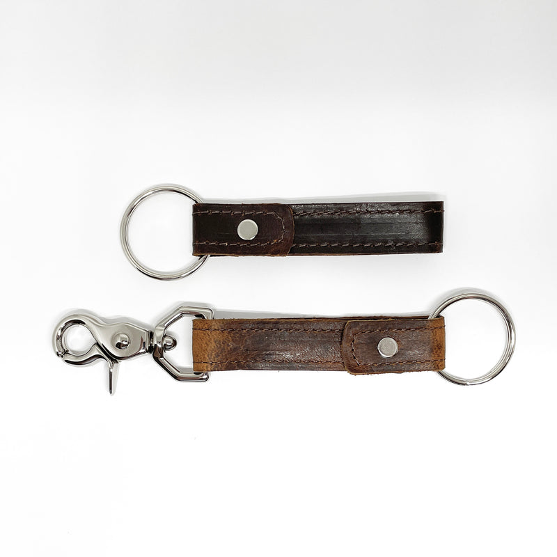 Two Tradevia brown leather keychains with a nickel rivet on a white background.