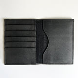 A monogrammed Tradevia black leather passport holder on a white surface.