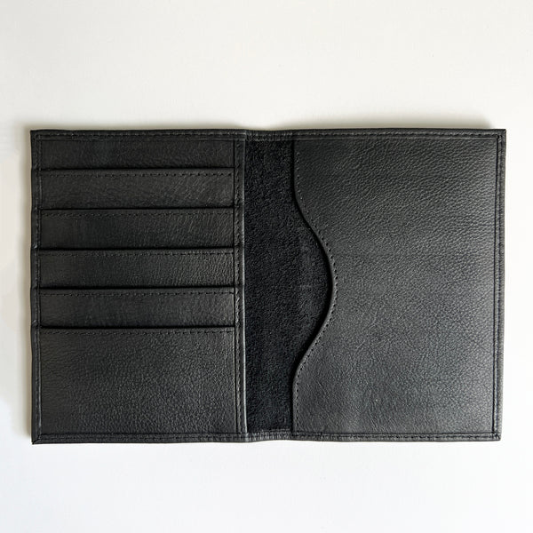 A monogrammed Tradevia black leather passport holder on a white surface.