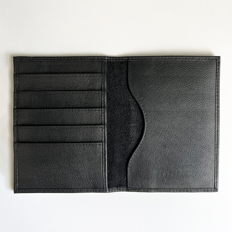 A monogrammed Tradevia black leather passport holder on a white surface.