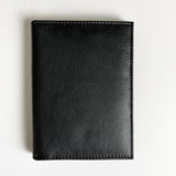 A black leather Tradevia passport holder with monogramming on a white surface, perfect for travelers.