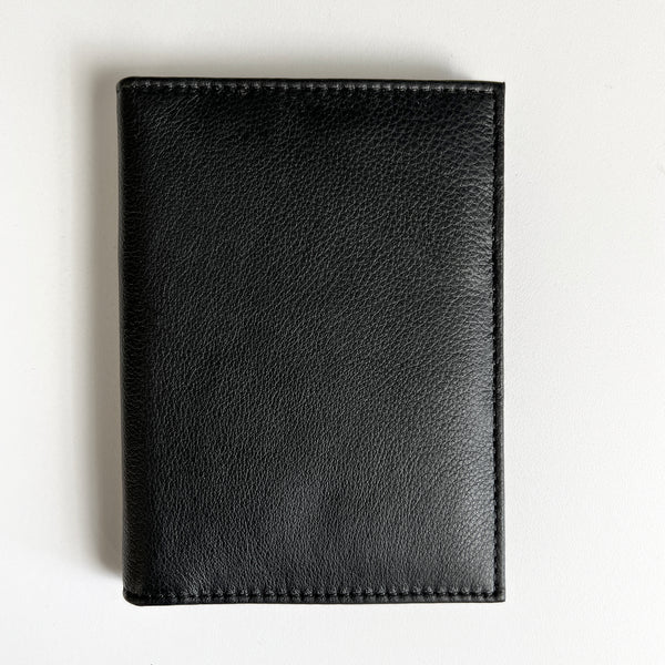 A black leather Tradevia passport holder with monogramming on a white surface, perfect for travelers.