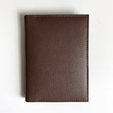 A Tradevia brown leather passport holder with monogramming on a white surface, perfect for travelers.