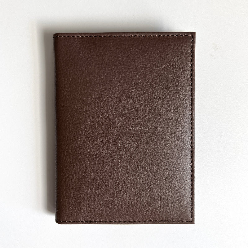A Tradevia brown leather passport holder with monogramming on a white surface, perfect for travelers.