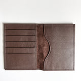 A monogrammed Tradevia brown leather passport holder on a white surface, perfect for travelers.