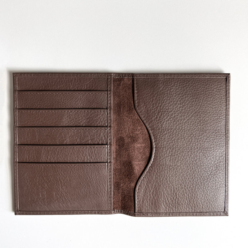 A monogrammed Tradevia brown leather passport holder on a white surface, perfect for travelers.