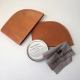 A tan leather wallet with a tin can of Tradevia All Natural Leather Cream and a cloth.