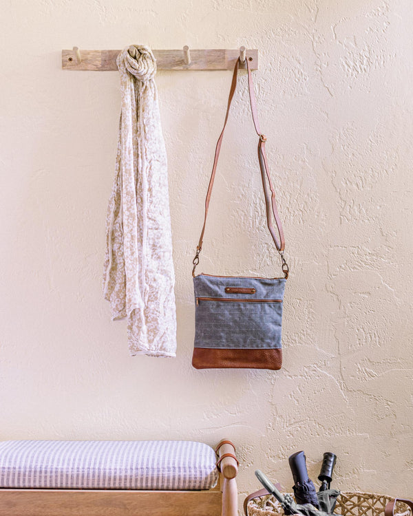 A bench with a bottle of wine and an Ellis River Crossbody Bag by Tradevia hanging on the wall.